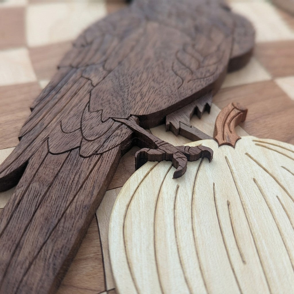 Close-up of a carved walnut raven’s tail and talon gripping a pale wood pumpkin with a copper-colored stem.
